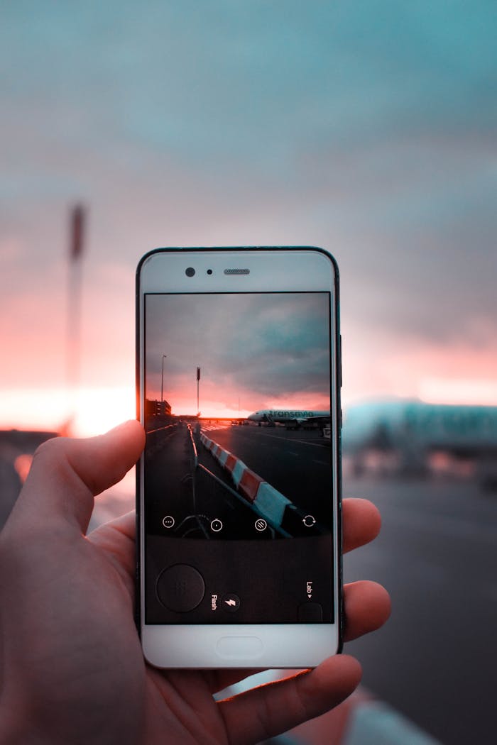 A hand holding a smartphone capturing a vibrant sunset scene with an open road.