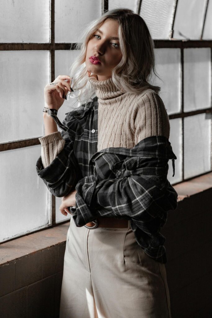 A stylish woman poses in layered fashion near a window, exuding modern elegance.