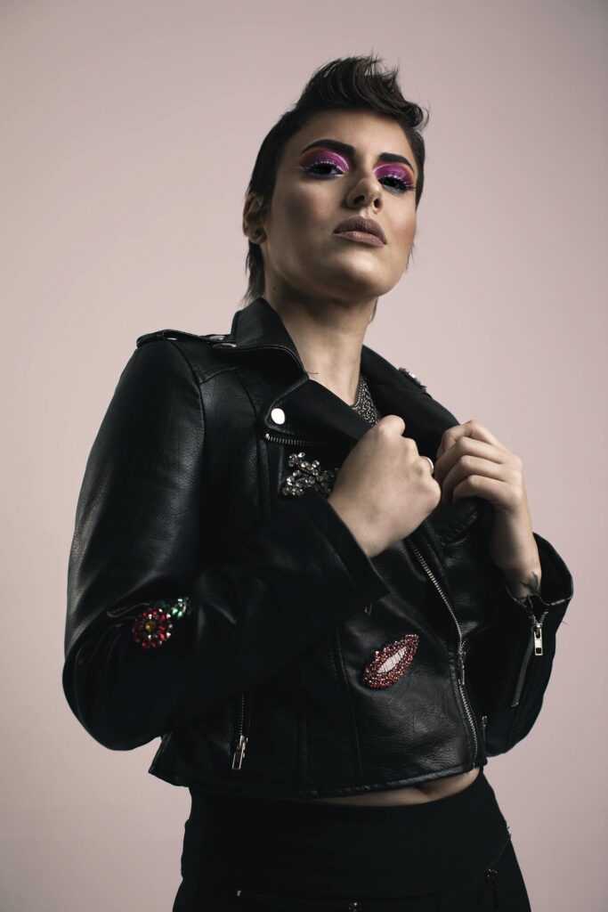 Fashion model posing with bold makeup and black leather jacket in studio.