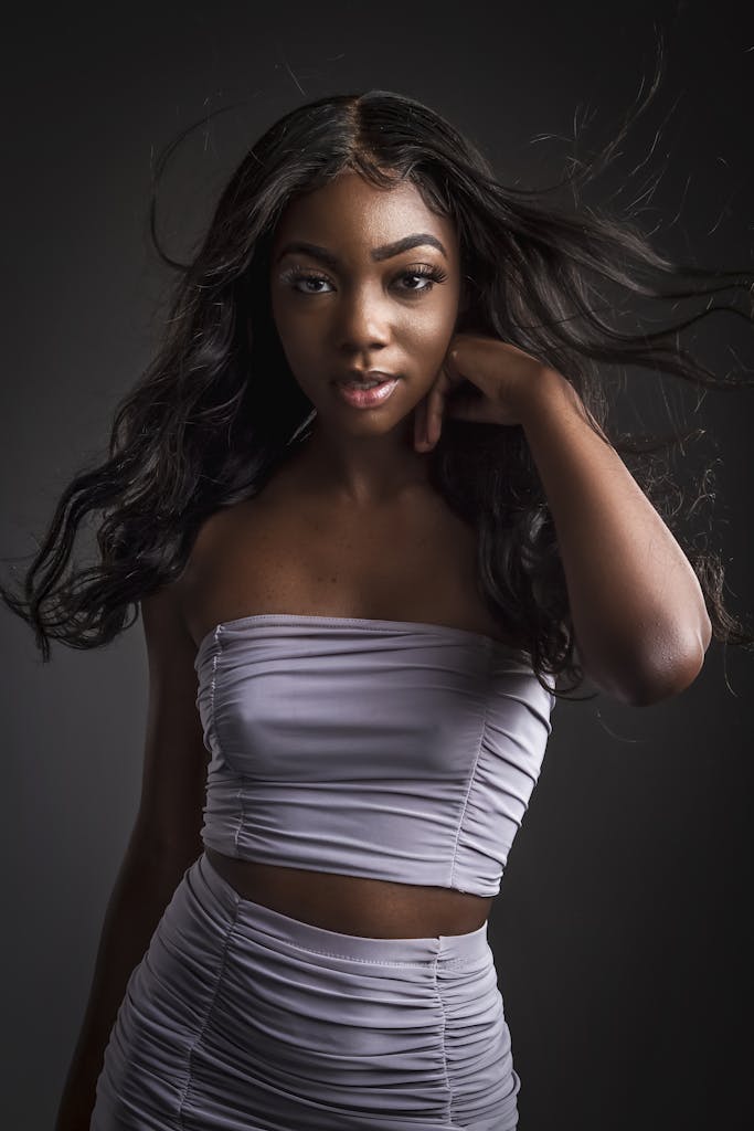 Studio portrait of a stylish woman in a white crop top, with hair flowing.